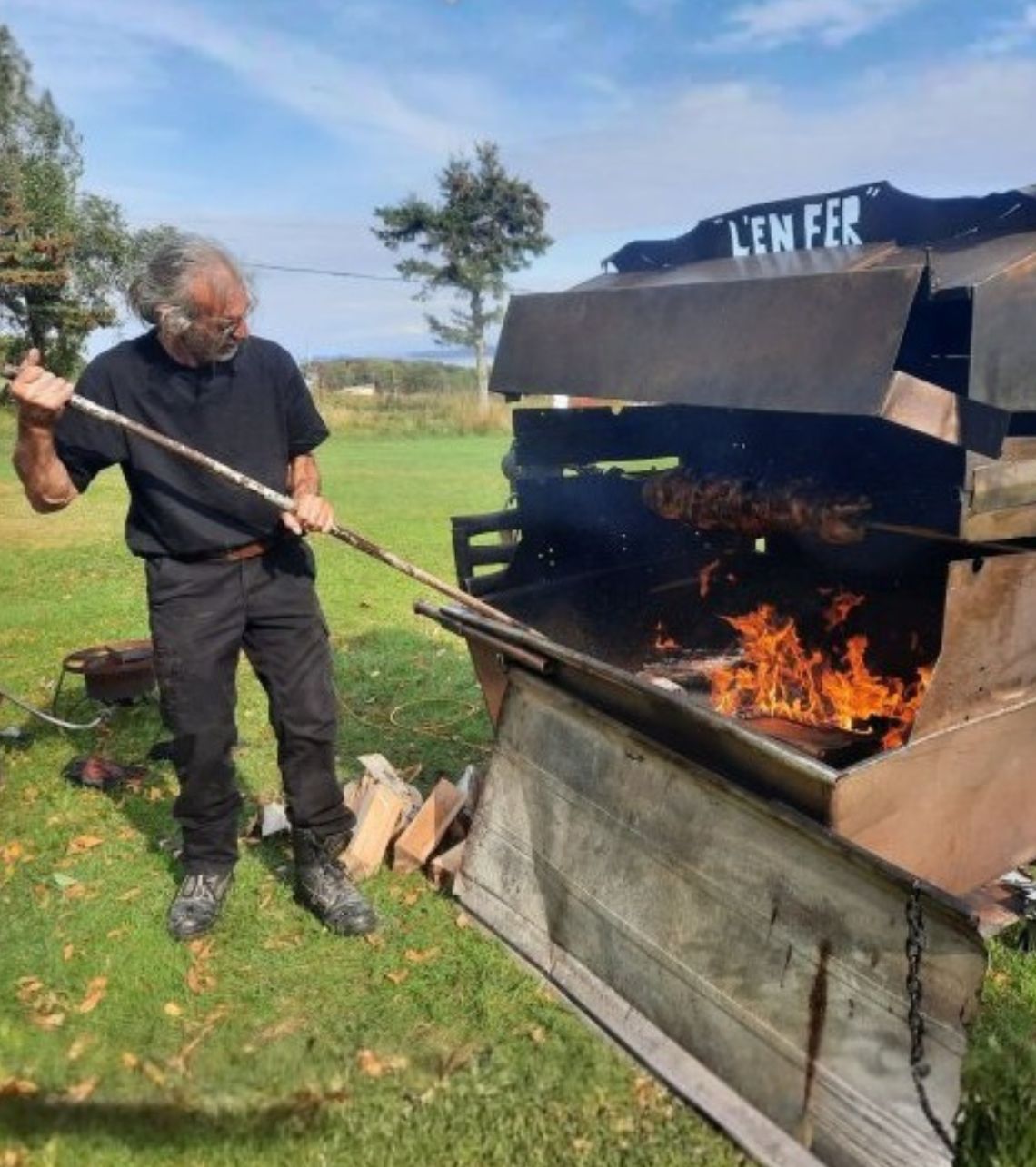 Chef de Méchoui du Marquis ajustant la cuisson au feu de bois pour un méchoui traditionnel en plein air au Québec, avec rôtissoire et viandes grillées pour évènements et réceptions